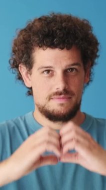 Yakından bakınca, kalbi parmak şeklinde temsil eden bir adam stüdyonun mavi arka planında izole edilmiş bir jest yapıyor.