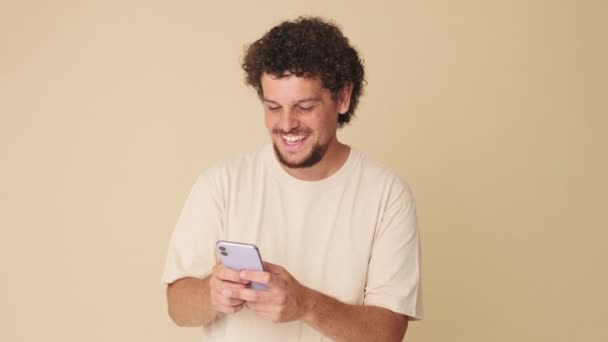 在米色背景下 拿着手机在工作室里笑的男人 — 图库视频影像