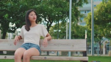 Genç kadın şehir parkında bankta otururken dinlenmekten zevk alıyor.