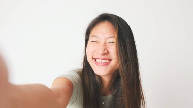 Gri bluzlu gülümseyen kız selfie çekiyor, beyaz arka planda video çekiyor, stüdyo çekimi.