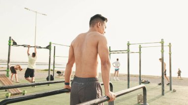 Guy, sporcu bir yaz günü açık hava spor sahasındaki paralel barlarda şınav çeker.