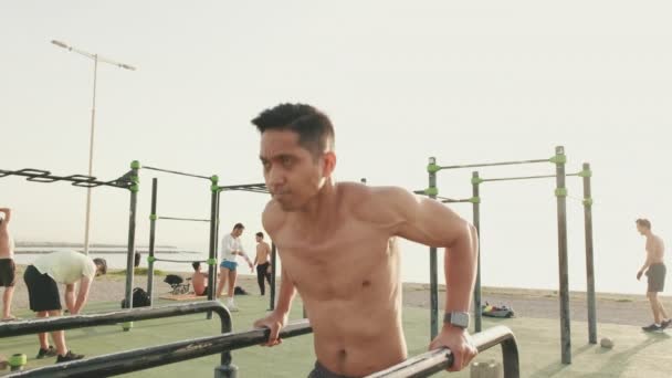 海のそばのスポーツ場の平行棒でプッシュアップを行う若い男 — ストック動画