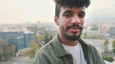 Balkonda dikilirken kameraya poz veren gülümseyen genç adamın yakın çekimi.