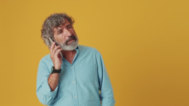 Irriterad Äldre Gråhårig Man Talar Mobiltelefon Isolerad Orange Bakgrund — Stockvideo