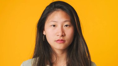 Yakın plan, gri bluzlu kız sarı arka planda izole edilmiş ve kameraya bakıyor.