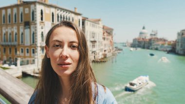 Venedik kanalının arka planında kameraya bakan güzel genç bir kadının yakın çekimi.