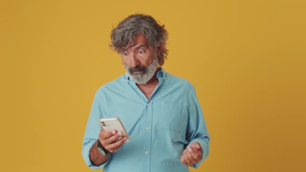 Šokovaný Starší Muž Ukazuje Telefon Při Pohledu Kameru Izolované Oranžovém — Stock video