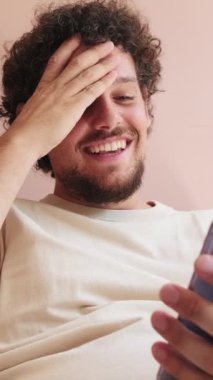 Oturma odasındaki kanepede oturan gülen adam telefon ekranına bakıyor.