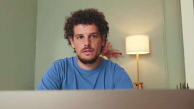 Oturma odasında oturan adam dizüstü bilgisayara bakıyor.