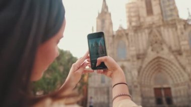 Kapanışta, kadın eski bir Avrupa şehrinin tarihi bölümünde dururken cep telefonuyla fotoğraf çekiyor.