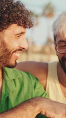 Yakın plan, homoseksüel çiftler sahilde otururken cep telefonlarıyla eğleniyorlar.