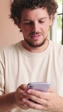 Oturma odasında beklerken cep telefonu kullanan gülümseyen adam.