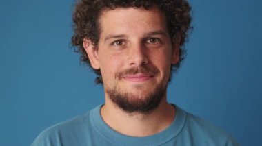 Mavi arka planda izole edilmiş bir gülümsemeyle kameraya bakan bir adam.