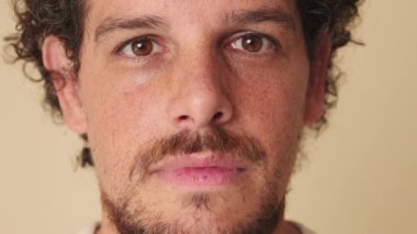 Bej arka planda gülümseyen stüdyoya bakan bir adamın yakın plan portresi.