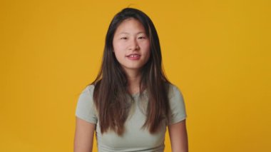 Genç bir kadın kameraya bakarken şaşkınlıkla el kaldırıyor. Stüdyoda sarı arka planda izole edilmiş.