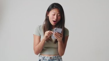 Genç bir kadın stüdyoda beyaz arka plan üzerinden izole edilmiş iyi mobil uygulamalar kullanıyor.