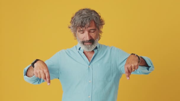 オレンジ色の背景に隔離された広告スペースで指を指す高齢の灰色の髪の男 — ストック動画