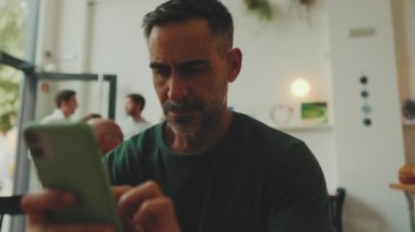 Orta yaşlı bir adam kafede oturmuş cep telefonuna mesaj yazıyor.
