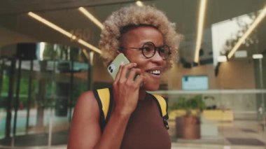 Sırt çantalı gülümseyen kadın sokakta dururken cep telefonuyla konuşuyor.