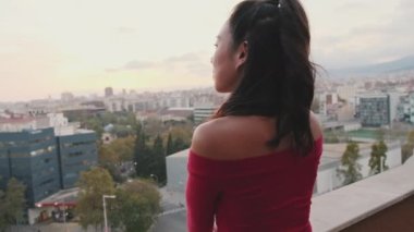 Gün batımında balkonda durup şehre bakan genç bir kadın.