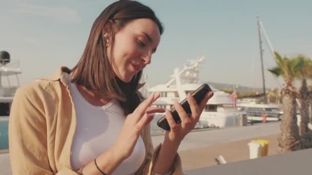 女性の旅行者はヨットの背景にマリーナで携帯電話の座席を使用しています — ストック動画
