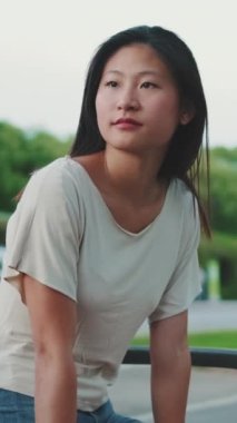 Genç bir kadın bankta oturuyor, etrafa bakıyor.