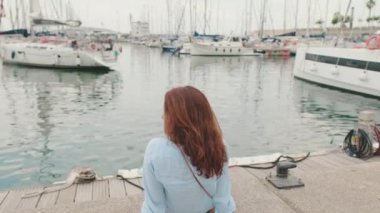 Güzel orta yaşlı kadın limanda oturur ve yatlara bakar.