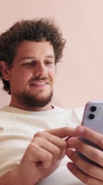 Oturma odasındaki kanepede oturan ve telefonu kullanan gülümseyen adam.