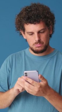 Elinde telefonla stüdyoda mavi arka planda baş parmak gösteren şaşırmış bir adam.