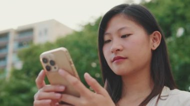 Yakından bakınca, genç kadın şehir parkında bankta oturuyor, cep telefonu kullanıyor.