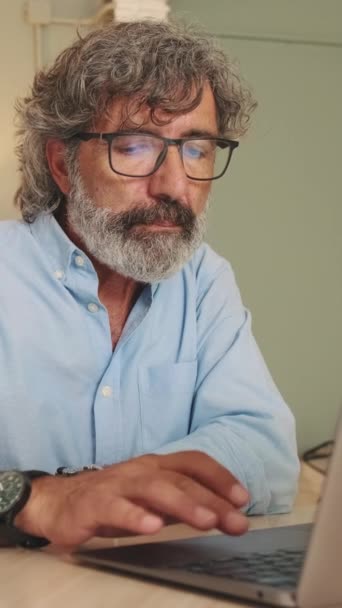 ラップトップで作業するリビングルームに座っているメガネで疲れた中年男性 — ストック動画
