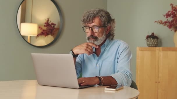 ラップトップコンピュータを使用してリビングルームに眼鏡をかけた高齢男性 — ストック動画