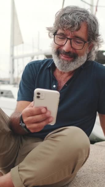 Uśmiechnięty Mężczyzna Średnim Wieku Siedzi Porcie Używając Telefonu — Wideo stockowe