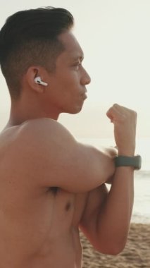 Genç atletik adam sahilde durup ısınıyor.