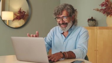 Oturma odasında gözlüklü mutlu yaşlı adam çevrimiçi video görüşmesi yapıyor.