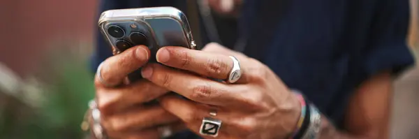 Erkek eli kelepçeli ve yüzüklü. Adam cep telefonu kullanıyor. Adam akıllı telefonuna mesaj yazıyor.