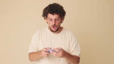 Çevrimiçi video oyunu oynayan adam kazanır, bej arka planda el sallar.