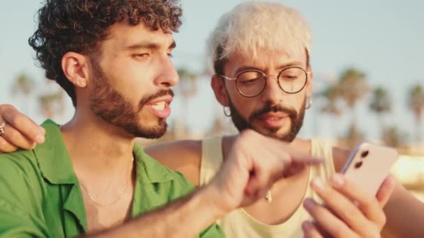 Zbliżenie Homoseksualiści Para Pomocą Telefon Komórkowy Podczas Siedzi Plaży — Wideo stockowe