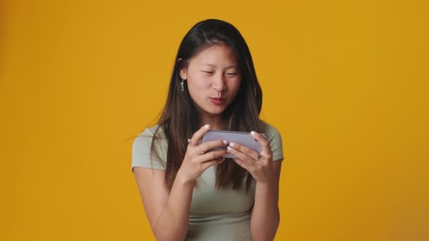 Smiling Young Woman Playing Mobile Phone Isolated Yellow Background Studio — Stock Video