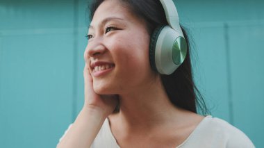 Kulaklık takmış, günlük giysiler giymiş, müzik dinleyip şarkı söyleyen güzel bir esmer kız.