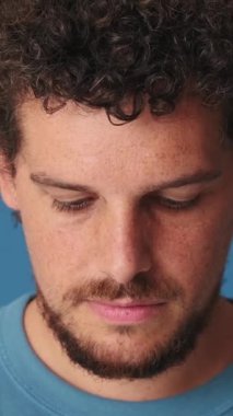 Yakın plan, adam kafasını kaldırıyor ve mavi arka planda izole edilmiş bir gülümsemeyle kameraya bakıyor.