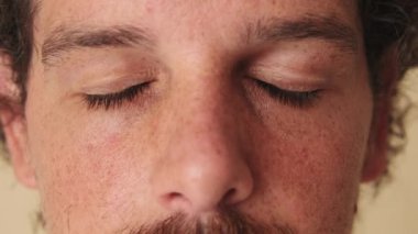 Gözünü açıp stüdyodaki bej arka plandaki kameraya bakarken çekilmiş detaylı bir yakın çekim.