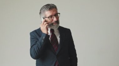 Akıllı telefondan konuşan mutlu işadamı, gri arka planda izole edilmiş, iyi haberler alıyor.