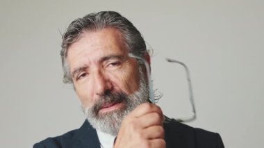 Gri arka planda izole bir şekilde kameraya bakan iş adamının gözlüğünü çıkardığı yakın plan.