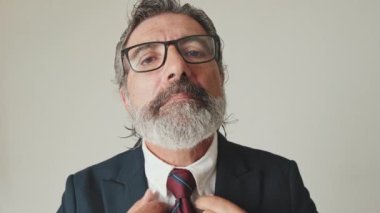 Yakın plan, iş adamı kravatını düzeltiyor aynada, gri arka planda kameraya bakıyor gibi bakıyor.