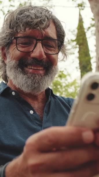 Primer Plano Del Anciano Sonriente Usando Teléfono Mientras Está Sentado — Vídeos de Stock