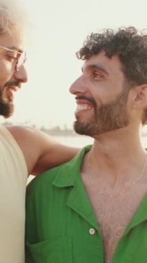 Eşcinsel erkekler birbirlerine sarılıp, dönüp kameraya gülümseyerek bakarlar.