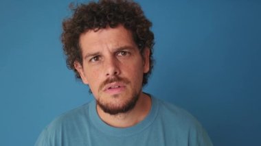 Kameraya bakıp mavi arka planda izole edilmiş bir şey arayan şaşırmış bir adamın yakın çekimi.