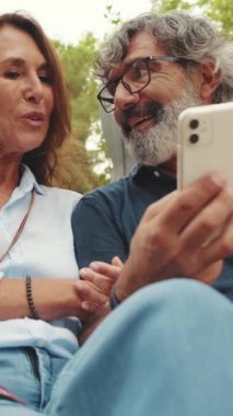 Yaşlı çift parkta otururken cep telefonu kullanırken iyi eğlenceler.