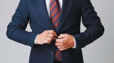 Yakın plan, tanınmayan iş adamı, gri arka planda izole edilmiş, takım elbisesini ayarlıyor.